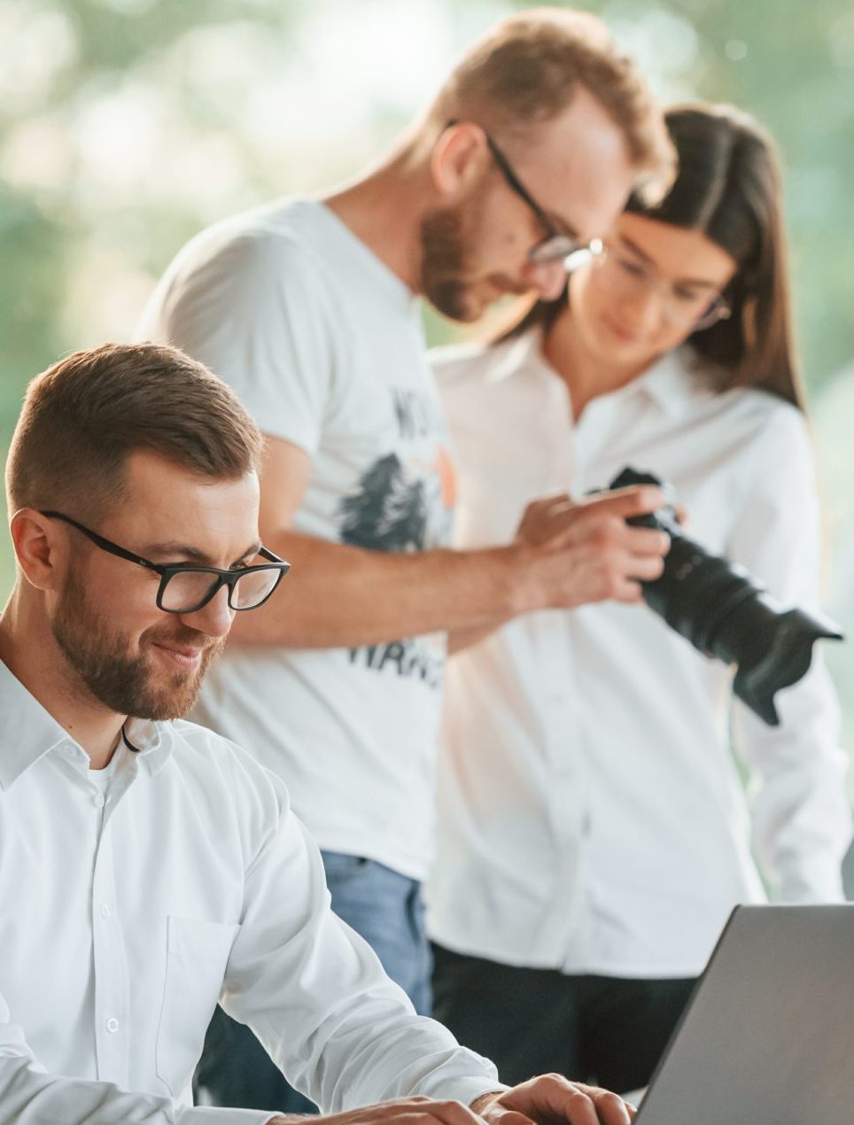 Man showing photos on the camera to a woman. Three people in formal clothes are working in the modern office together